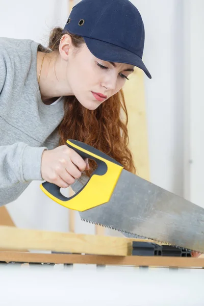 Junge Handwerkerin schneidet mit der Handsäge ein Holzbrett — Stockfoto