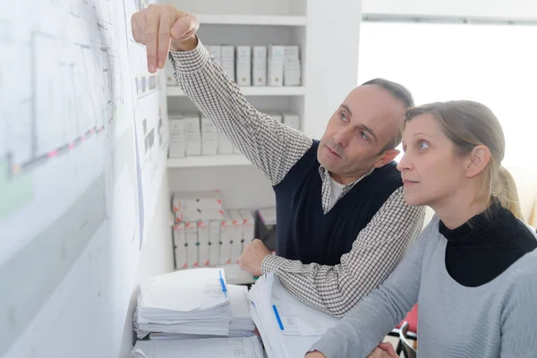 Man and woman looking at paperwork pinned on the wall — Stock Photo, Image