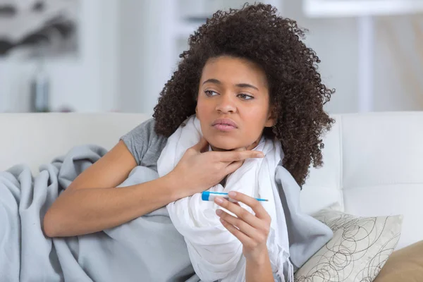 Lady at home holding her throat and a thermometer — Stock Photo, Image