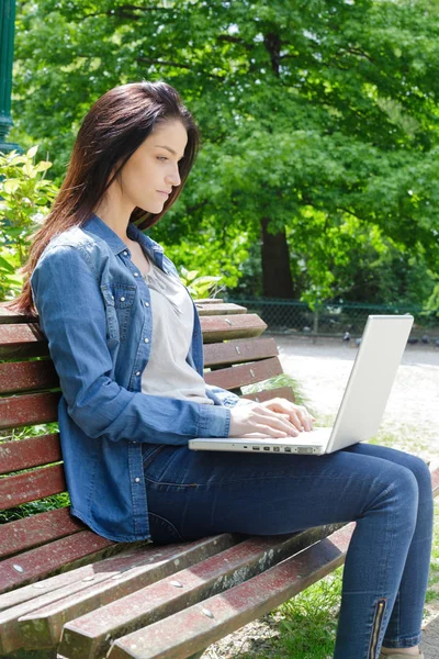 Chica joven en un banco con un ordenador portátil — Foto de Stock