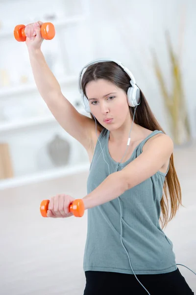 Mujer joven haciendo ejercicio con pesas, usando auriculares — Foto de Stock