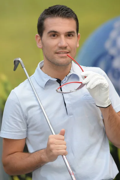Sorridente giovane uomo che trasporta borsa da golf mentre in piedi sul campo — Foto Stock