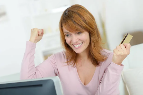 Happy middle aged woman using computer and holding credit card — Stock Photo, Image