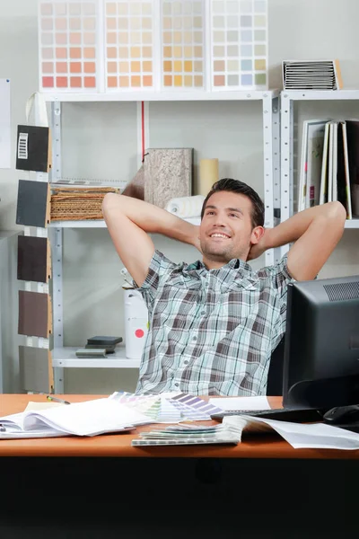 Hombre sonriente en el escritorio con las manos detrás de la cabeza —  Fotos de Stock