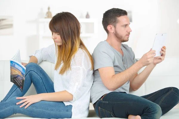 Pareja sentada espalda con espalda leyendo libro y tableta pantalla —  Fotos de Stock