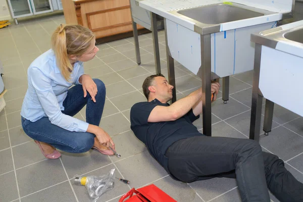 Jonge vrouw kijken loodgieter vaststelling aanrecht — Stockfoto