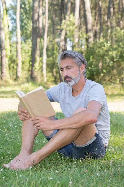 Adam lyingsitting bir kitap okuma çim — Stok fotoğraf