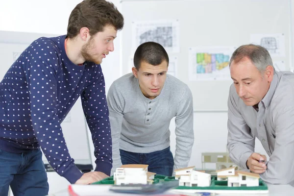 Arquitectos sonrientes con modelo de casa y plano trabajando en la oficina —  Fotos de Stock