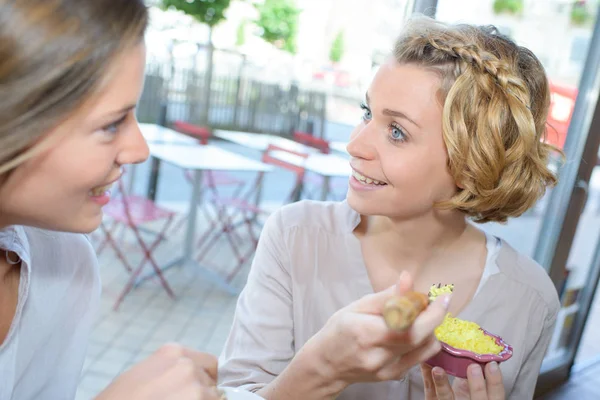 Duas jovens mulheres rindo e comendo em um café — Fotografia de Stock