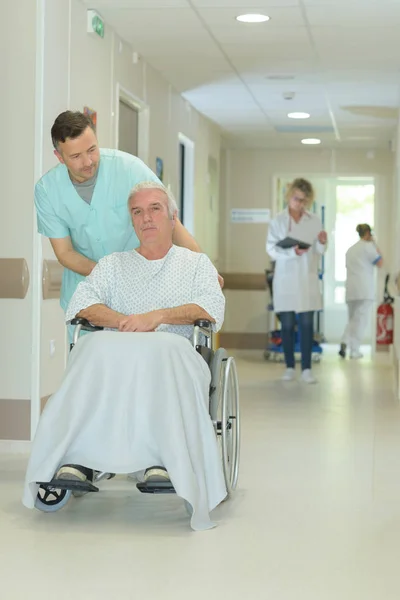 Doctor and senior man patient in wheelchair at hospital corridor — Stock Photo, Image