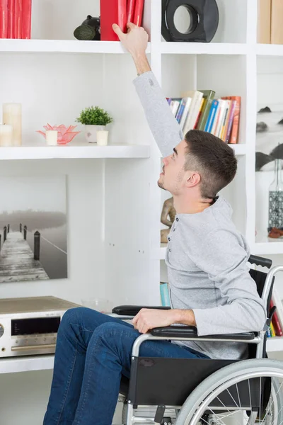 Uomo sulla sedia a rotelle che raggiunge per un libro — Foto Stock