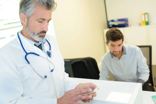 Médico consultando su teléfono durante la consulta con un paciente —  Fotos de Stock