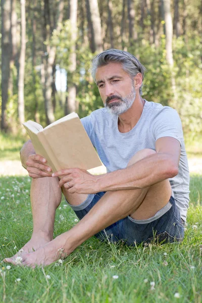 Hombre acostado en la hierba leyendo un libro — Foto de Stock