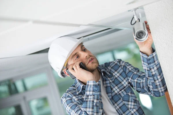 Auftragnehmer Überprüft Überwachungskamera Und Telefoniert — Stockfoto