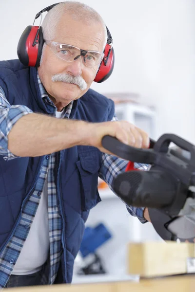 年配の男性が丸鋸を使用している間耳プロテクターを装着 — ストック写真