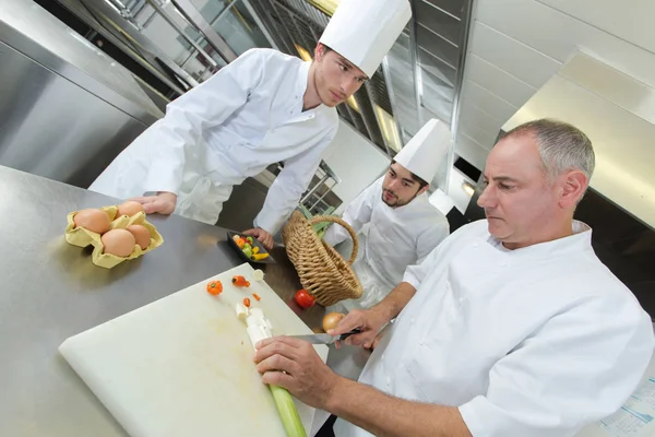 Assistentes de chef assistindo seu chefe preparando um prato — Fotografia de Stock