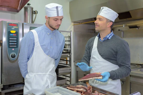 Leerling en chief voorbereiding van vlees in restaurant keuken — Stockfoto