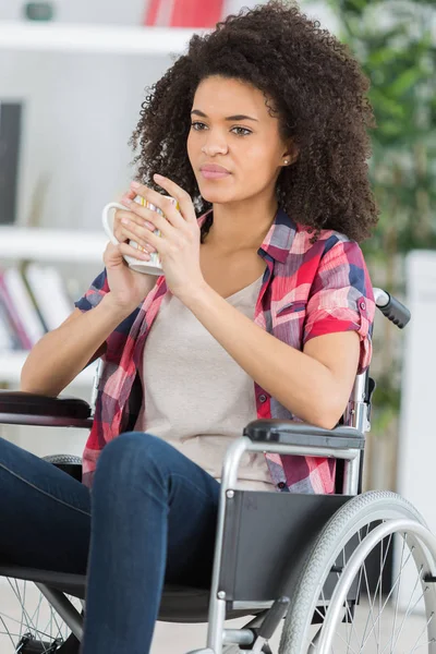 Девушка в инвалидной коляске с чашкой в руках — стоковое фото