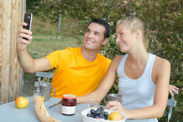 Casal tomando selfie enquanto toma café da manhã ao ar livre — Fotografia de Stock