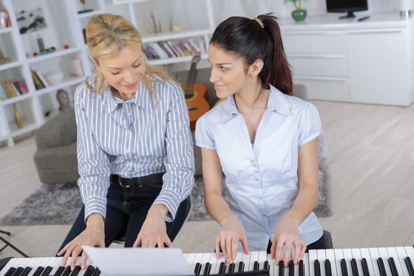 Moeder en dochter glimlachend en een piano thuis spelen — Stockfoto