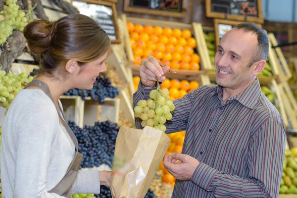 Menina morena vendendo frutas maduras para cliente masculino no supermercado — Fotografia de Stock