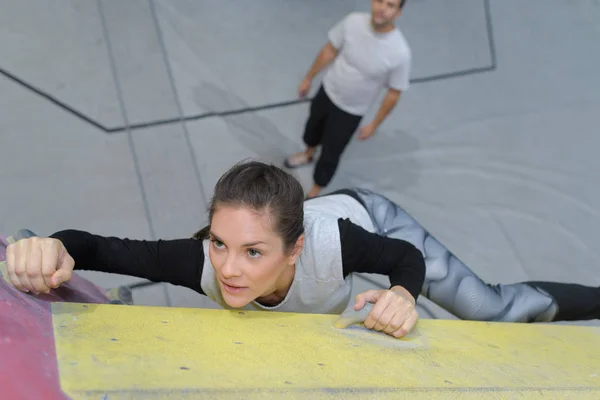 Mujer joven practicando escalada en roca en una pared de roca en el interior — Foto de Stock