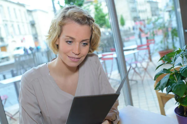 Vacker kvinna sitter vid bord i café läsa menyn — Stockfoto