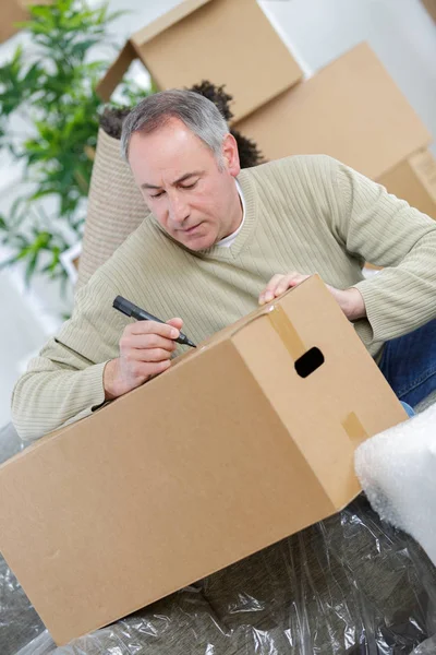 Glücklicher Mann zieht in neues Haus und schreibt auf Schachtel — Stockfoto