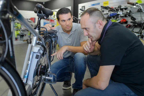 Hombre comprueba bicicleta antes de comprar en la tienda de deportes — Foto de Stock