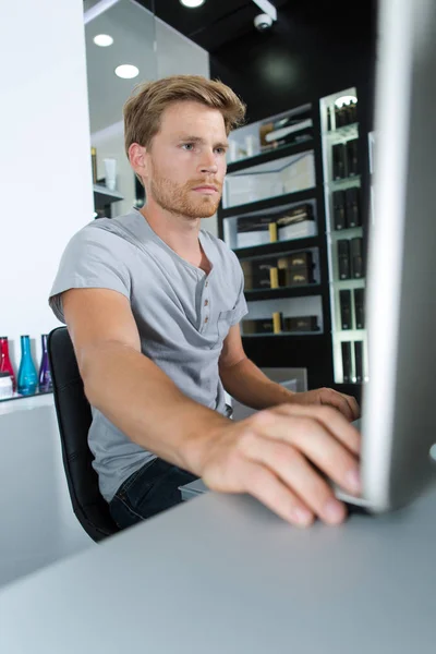 Glücklicher junger Mann benutzt PC im Friseursalon — Stockfoto