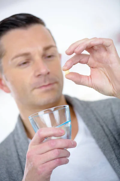 Όμορφος άνδρας με χάπι και το ποτήρι του νερού στο σπίτι — Φωτογραφία Αρχείου