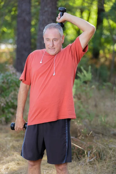 Middle-age man with dumbbells on a lawn — Stock Photo, Image