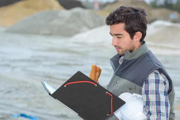 Homme regardant le dossier, mangeant un sandwich — Photo