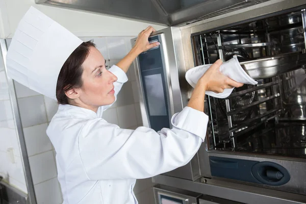 工業用オーブンで何かを置く女性シェフ — ストック写真