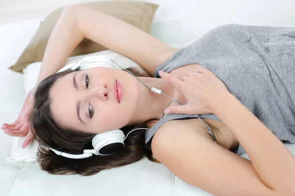 戴着耳机的年轻女性躺在床上 — 图库照片