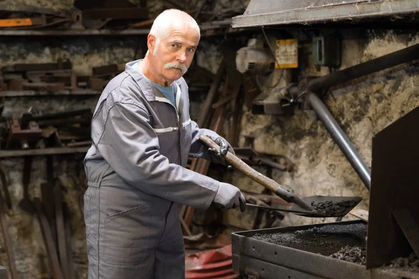 Senior blacksmith heats item before forgingin smithy — Stock Photo, Image