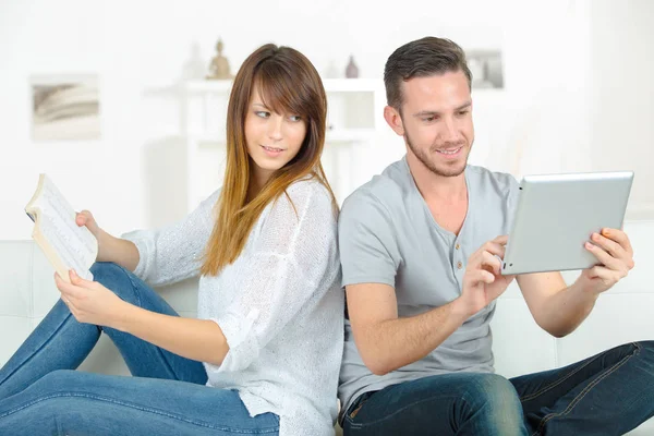 Sorrindo casal lendo ebooks no sofá em casa — Fotografia de Stock