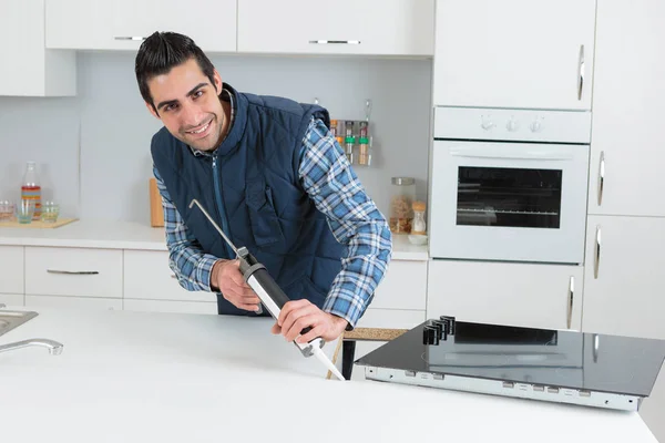 Plumber putting a silicone sealant in a kitchen — Stock Photo, Image