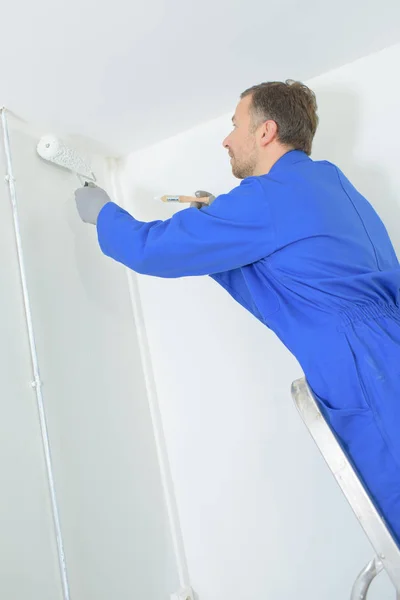 Pintor homem no trabalho com um rolo de pintura e escada — Fotografia de Stock