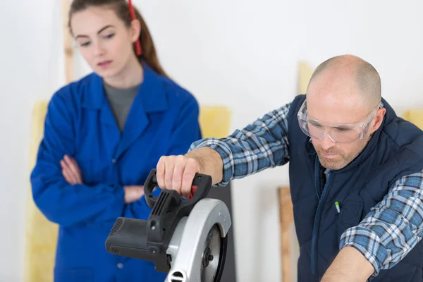 Carpenter showing apprentice how to cut a wooden plank — Stock Photo, Image