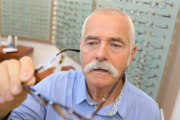 Starszy człowiek próbuje nowych okularów w sklepie optycznym — Zdjęcie stockowe
