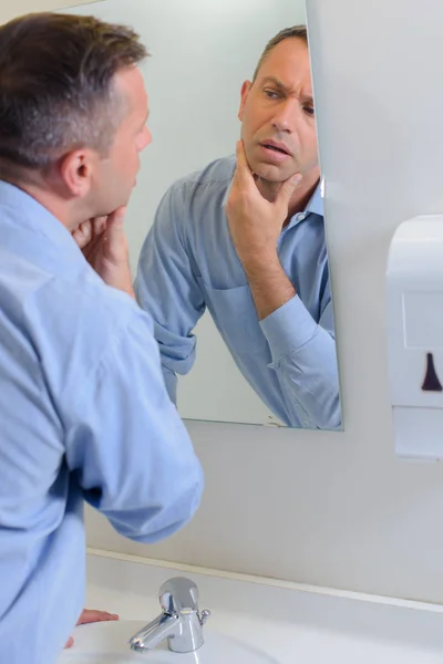 Man inspecting face in mirror — Stock Photo, Image
