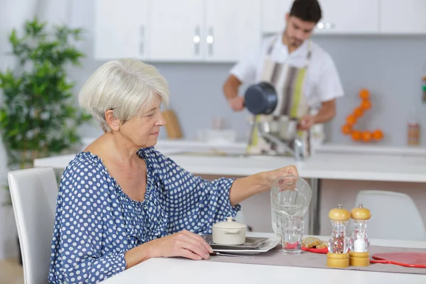 Glad ung man som serverar frukost till en äldre kvinna — Stockfoto