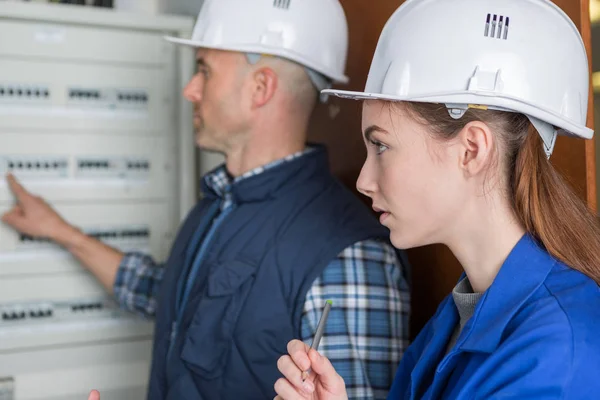 Mujer y maestro midiendo la corriente eléctrica de un tablero de fusibles — Foto de Stock