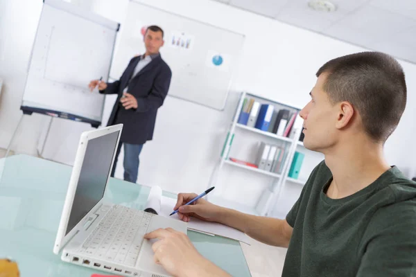 Hombre se puso de pie en el rotafolio estudiante se sentó usando portátil haciendo notas — Foto de Stock