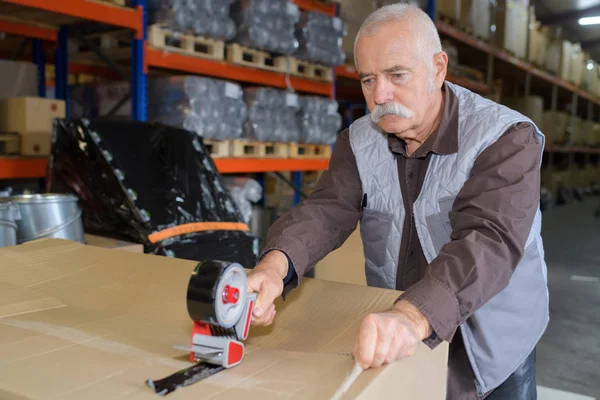 Lavoratore anziano che attacca una scatola in magazzino — Foto Stock