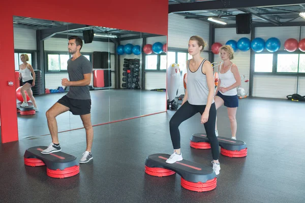 Young sporty people training with steppers in gym — Stock Photo, Image