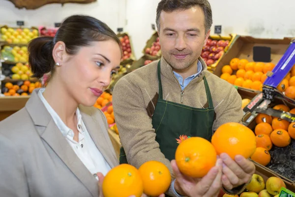 Mujer sonriente eligiendo diferentes frutas en la exhibición de la tienda de alimentos de granja —  Fotos de Stock