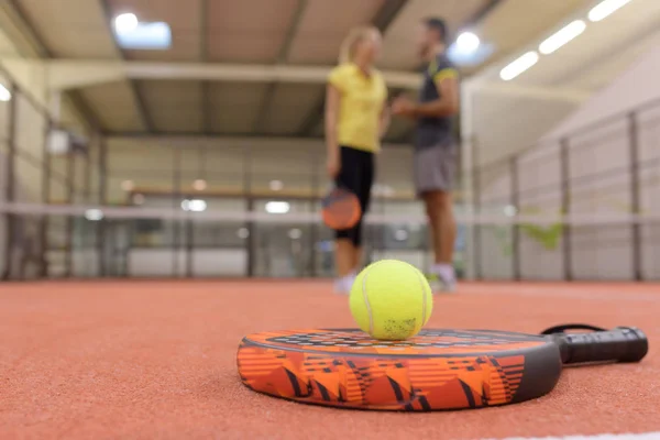 Raqueta de tenis y dos bolas cerca de la red en la cancha cubierta — Foto de Stock