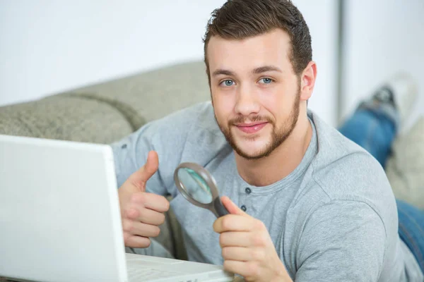 Homem na frente do laptop segurando lupa — Fotografia de Stock